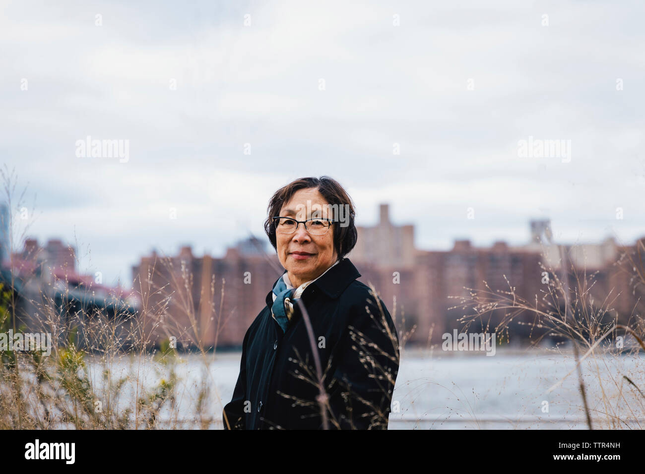 Portrait of smiling senior woman standing against cloudy sky in city Banque D'Images