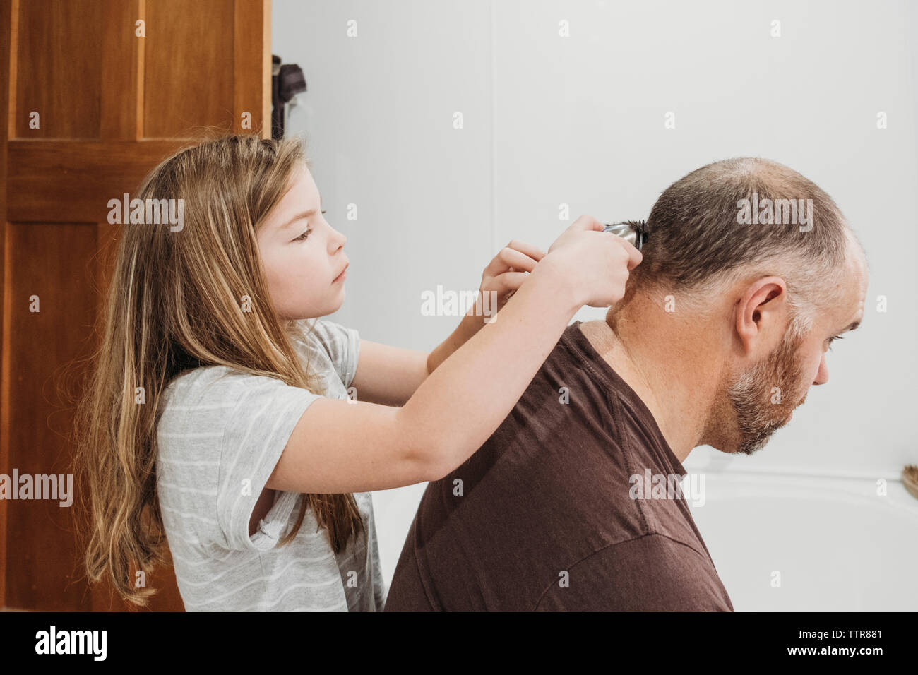 Jeune fille à l'aide de tondeuses pour couper les cheveux de son père Banque D'Images