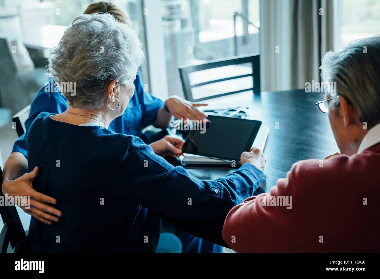 Aide familiale au cours de l'ordinateur tablette avec senior couple assis à table à manger Banque D'Images