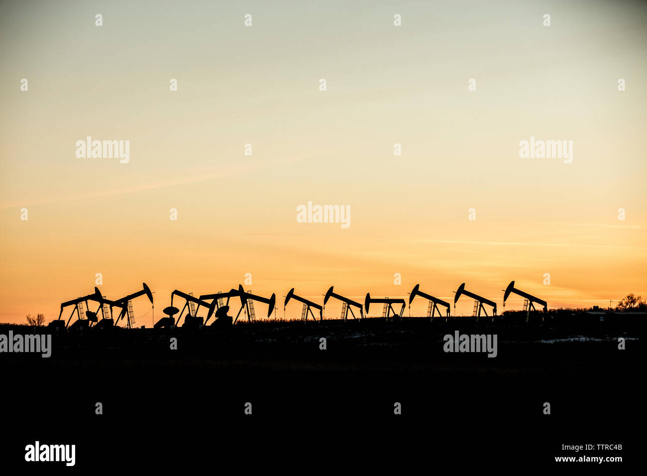 Vue à moyenne distance de silhouette chevalets à l'industrie de l'huile contre le ciel au coucher du soleil Banque D'Images