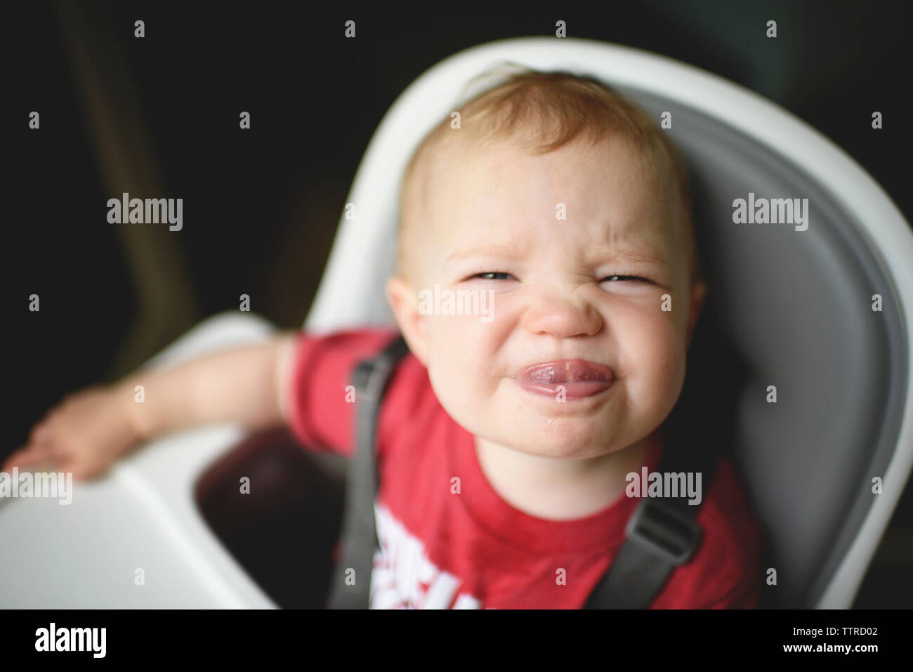 High angle portrait of cute baby girl sticking out tongue, assis sur une chaise haute à la maison Banque D'Images