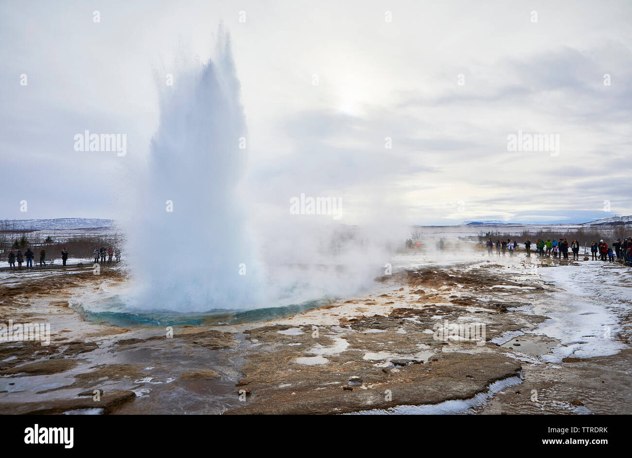 Les touristes à la recherche d'une projection d'eau à geyser contre ciel nuageux au cours de l'hiver Banque D'Images