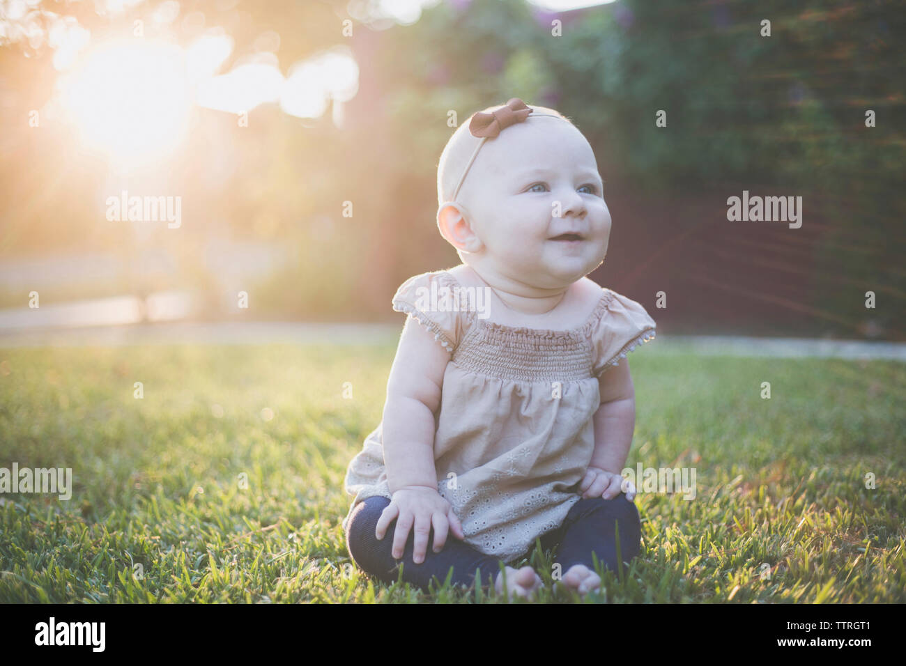 Happy baby girl looking away while sitting on grassy field à l'arrière-cour Banque D'Images