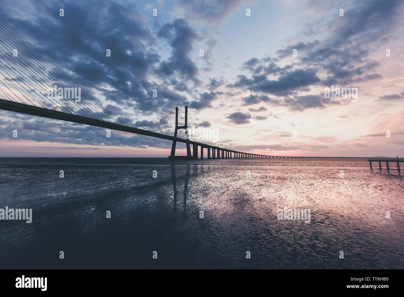 Silhouette Pont Vasco da Gama sur le fleuve Tage contre ciel nuageux au lever du soleil Banque D'Images