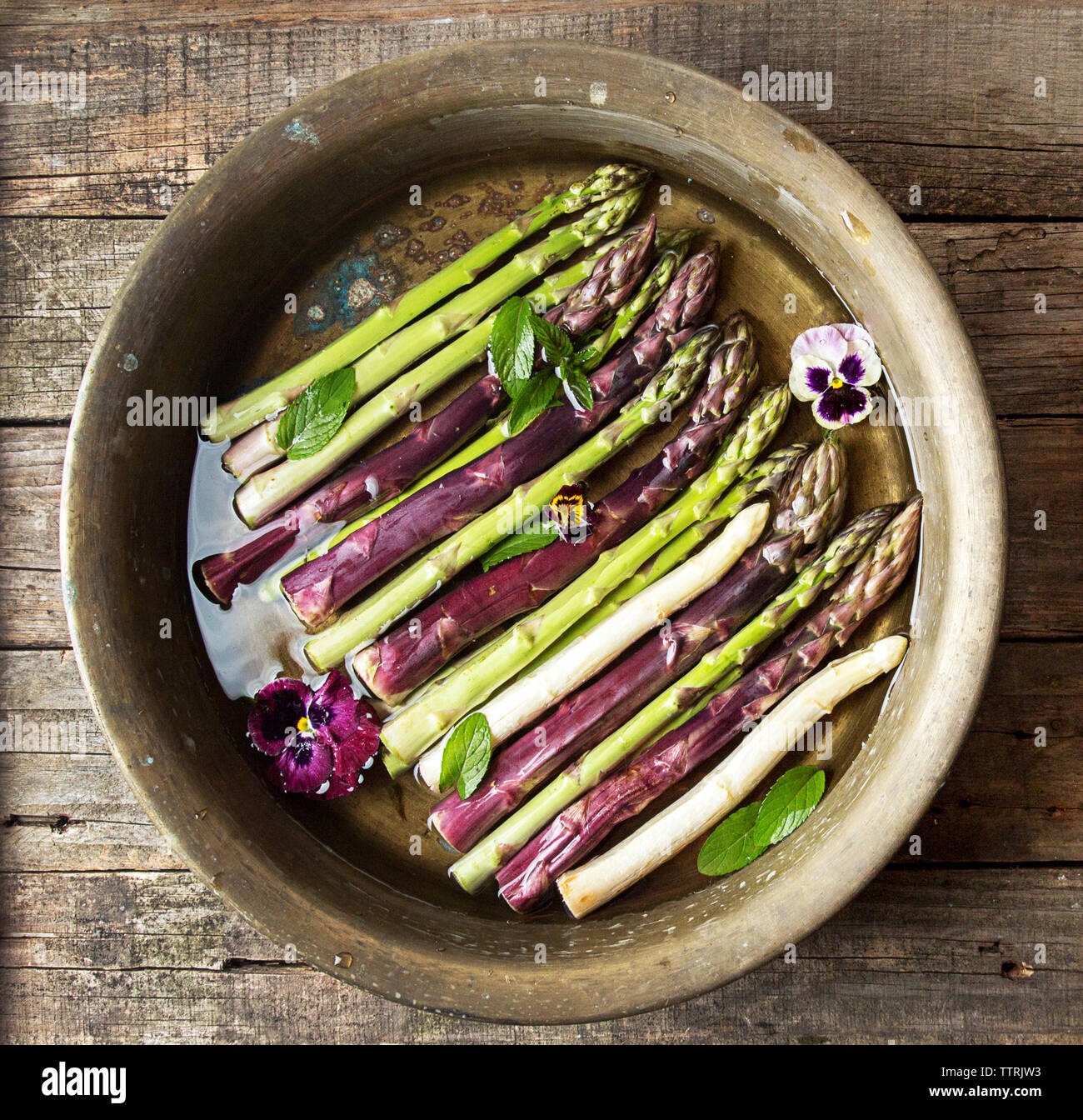 Vue de dessus de l'asperge avec des fleurs et des feuilles de menthe dans un bol de cuivre sur la table en bois Banque D'Images