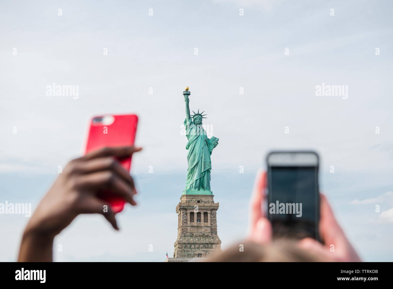 Les mains coupées à l'aide de téléphones intelligents à l'encontre de la Statue de la liberté et ciel nuageux en ville Banque D'Images