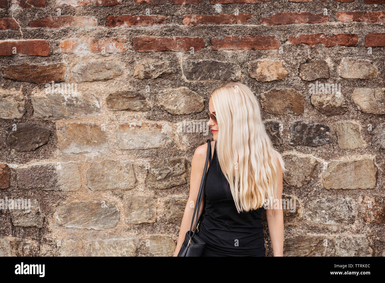 Femme aux cheveux blonds portant des lunettes de soleil en position debout contre l'ancien mur Banque D'Images