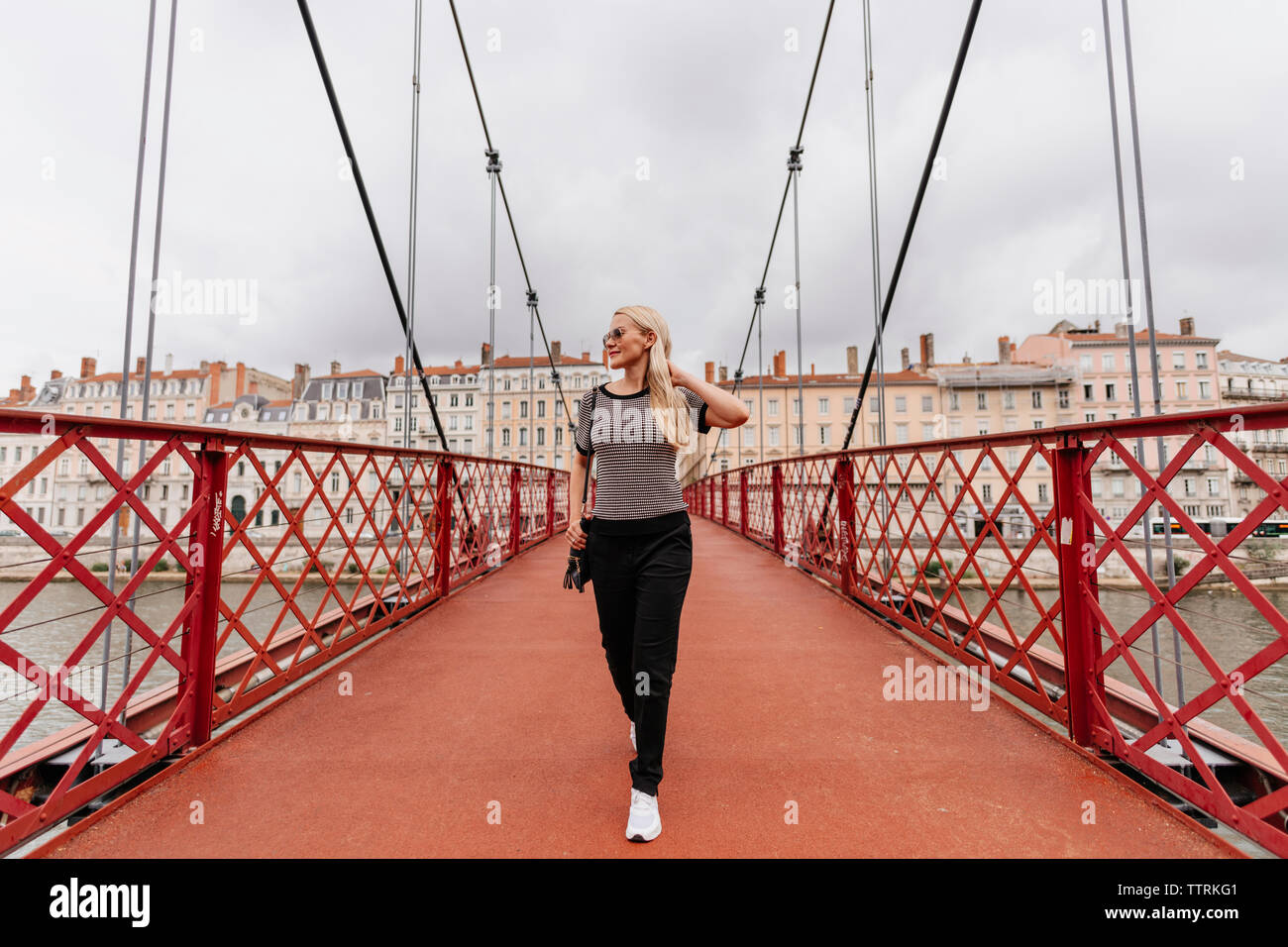 Woman with Blonde hair marche sur Passerelle Paul-Couturier contre les bâtiments en ville Banque D'Images