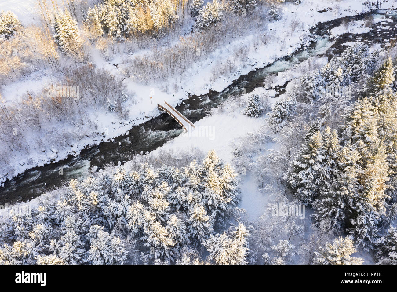 Drone vue sur la rivière d'exécution entre les bois et la campagne de conifères avec passerelle passerelle dans la neige en hiver Banque D'Images
