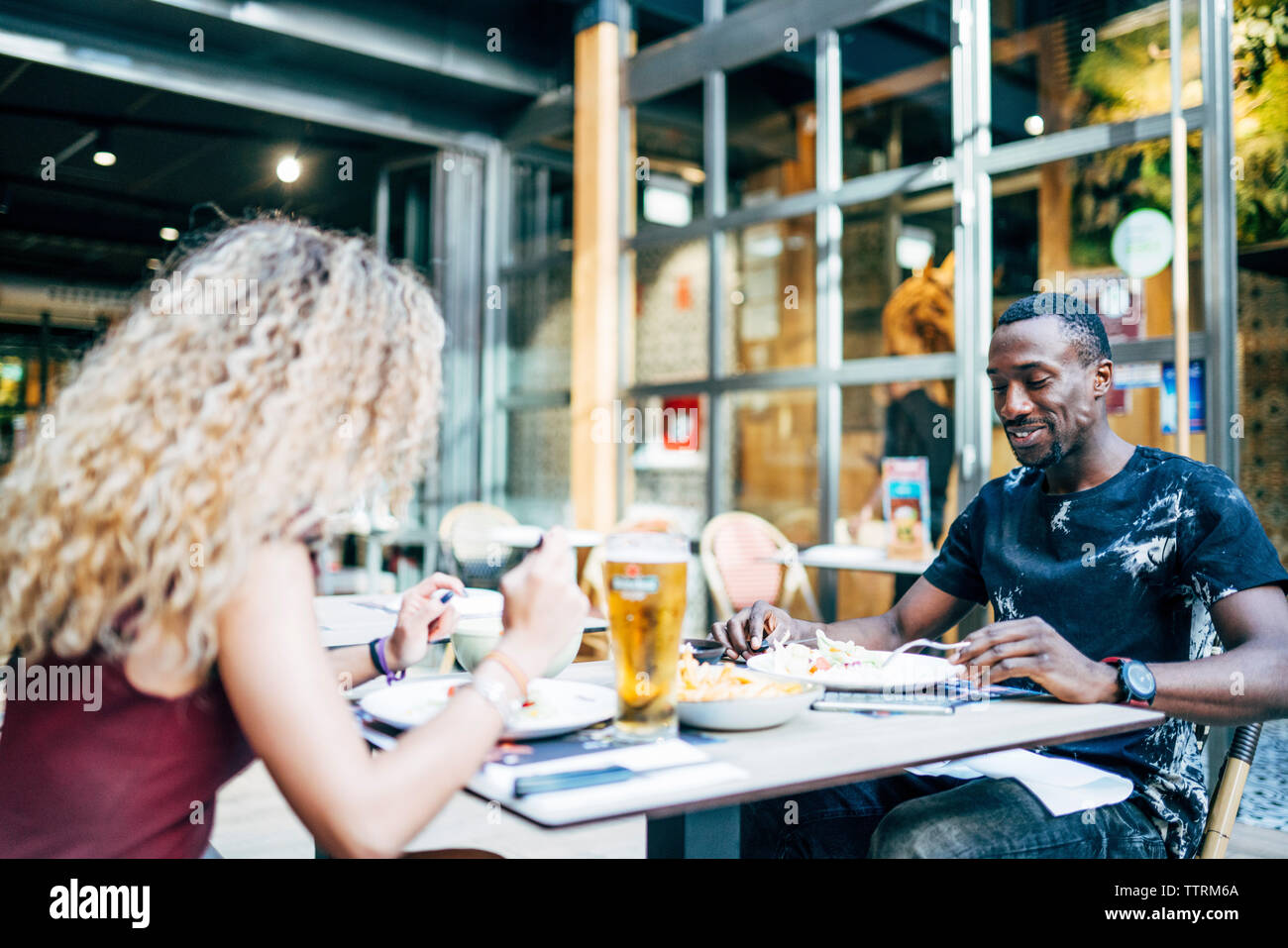 Femme blonde et l'homme africain aiment manger au restaurant. Banque D'Images
