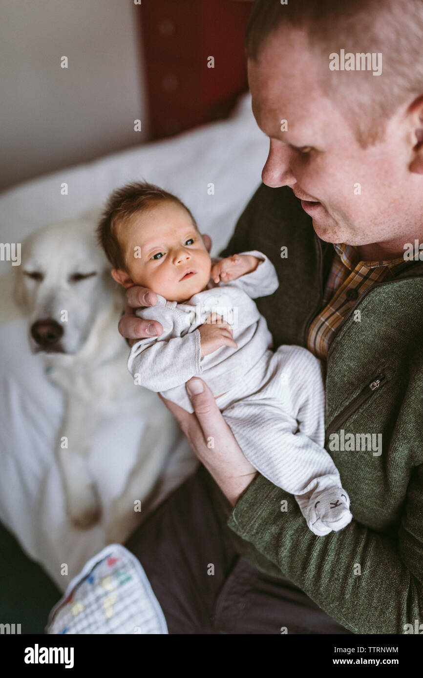 nouveau-père tenant la fille du nouveau-né sur le lit avec le chien en arrière-plan Banque D'Images