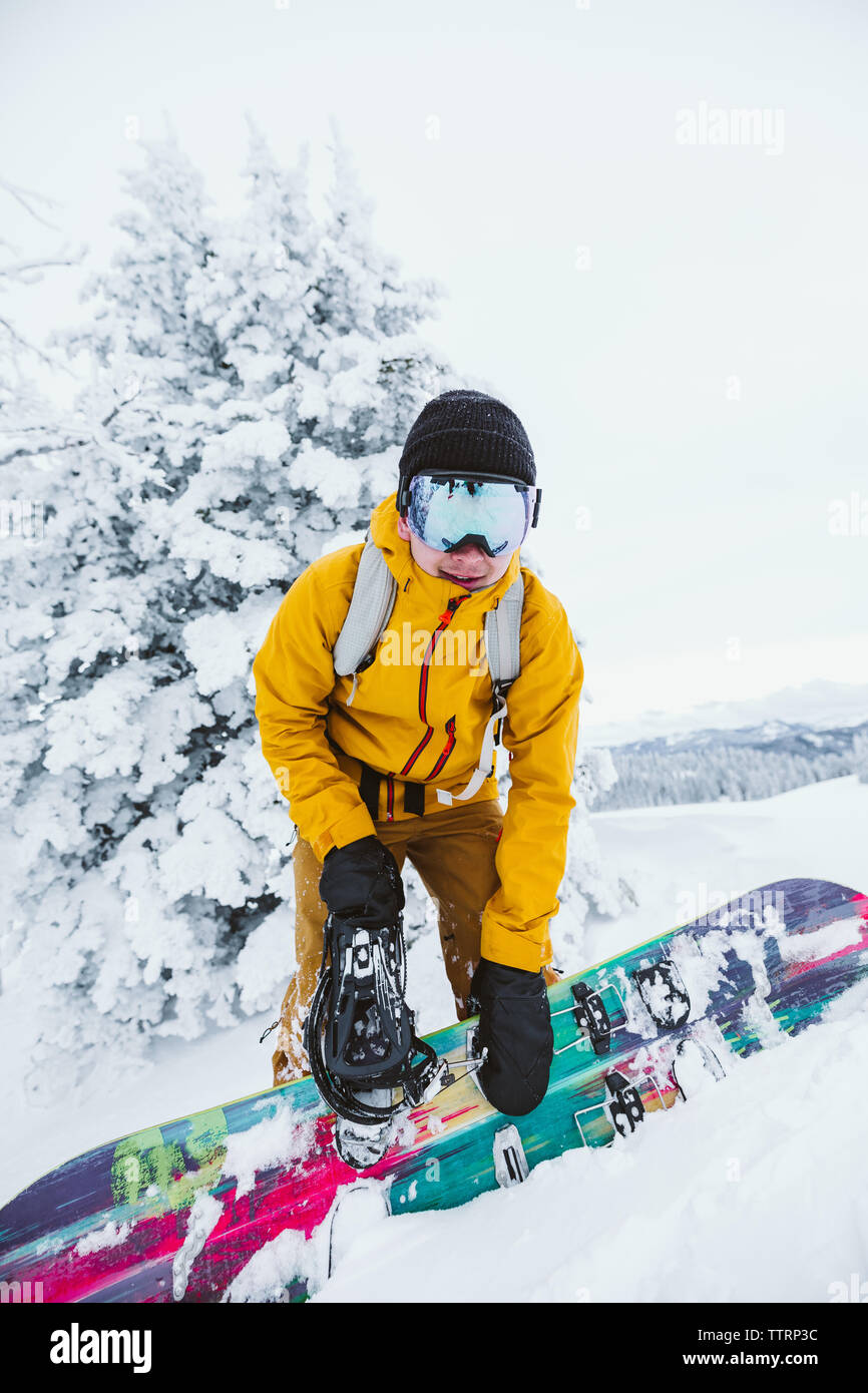 Jeune homme snowboarder dans yellow jacket ajuste son board Banque D'Images