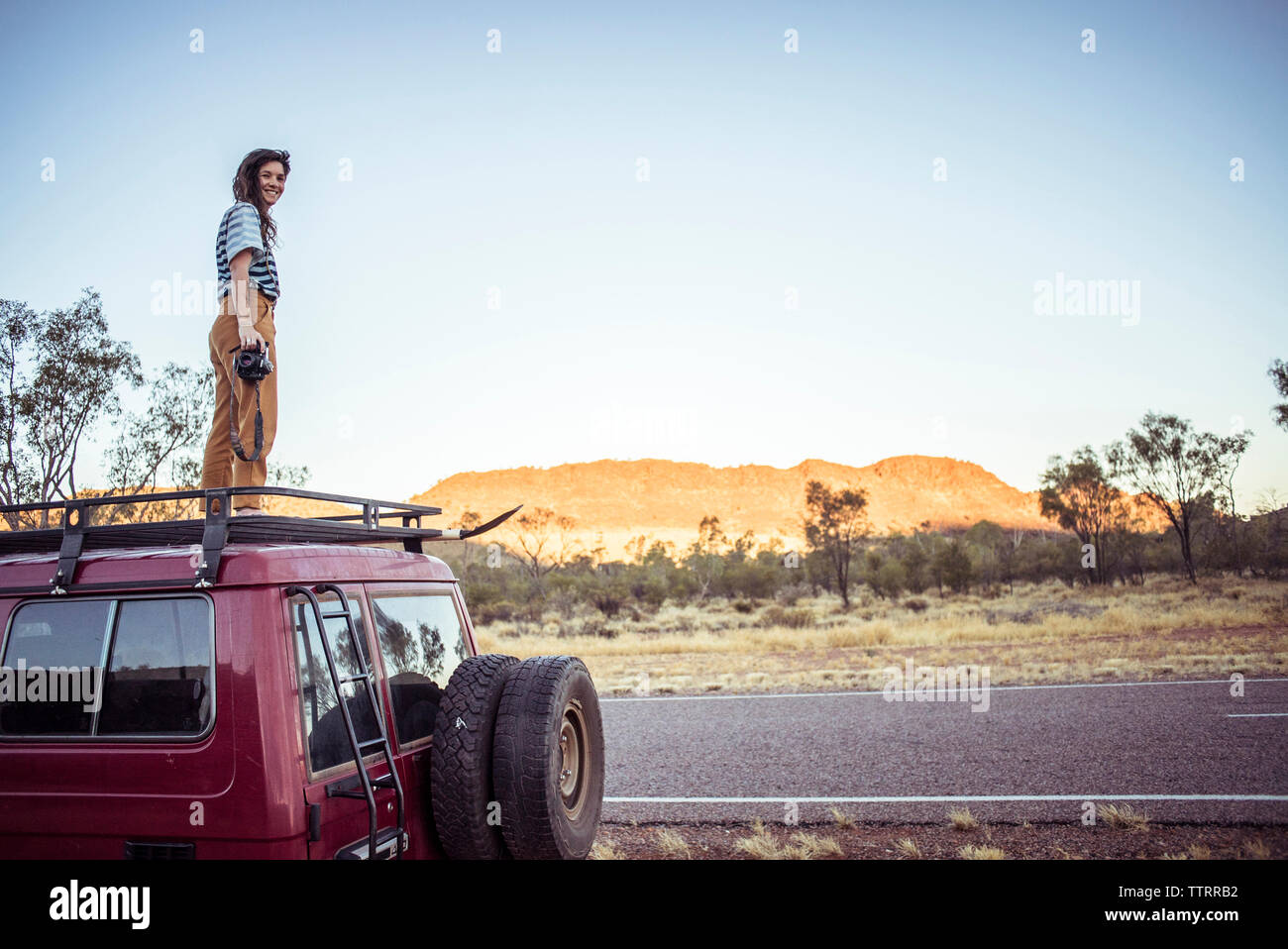 Portrait of smiling woman with camera debout sur toit de voiture dans le desert Banque D'Images