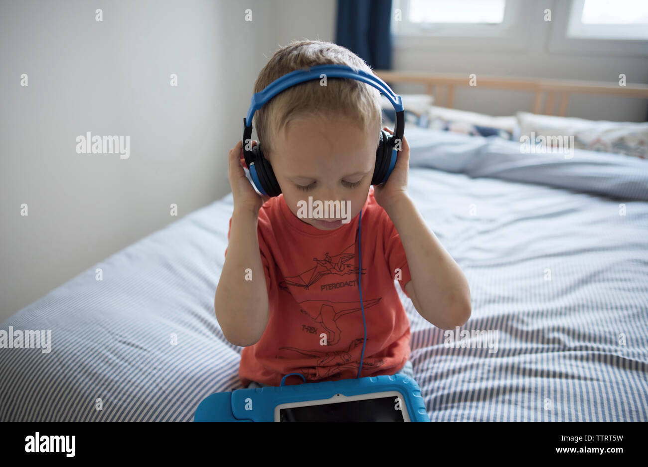 Portrait of boy listening music while sitting on bed at home Banque D'Images