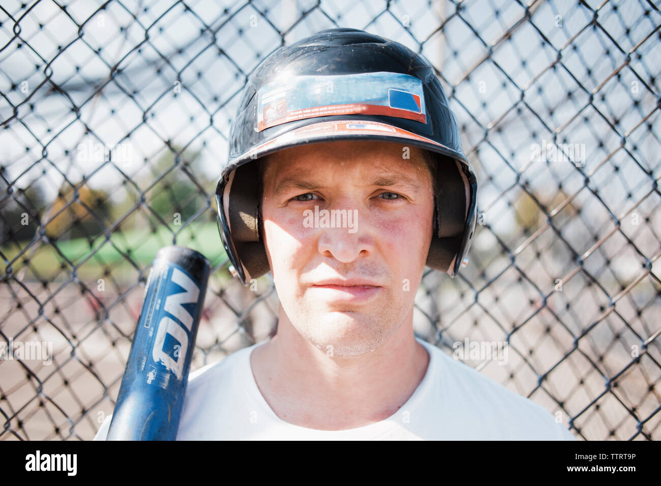 Close-up portrait of smiling woman wearing sports baseball casque contre acier clôture à égalité au cours de journée ensoleillée Banque D'Images