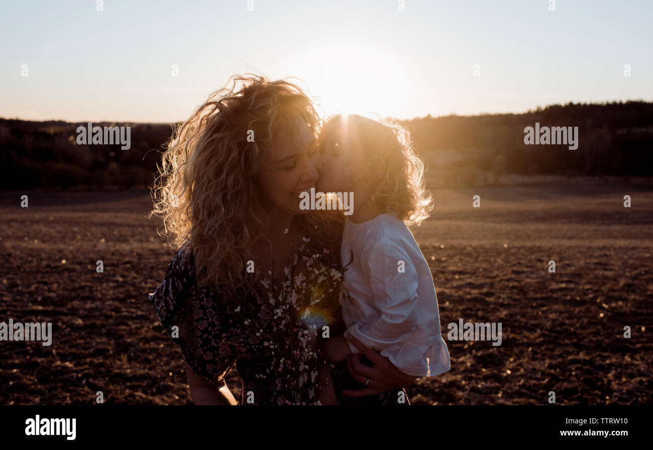 Fille aimante mère joyeuse embrasser tout en étant transporté sur terrain pendant le coucher du soleil Banque D'Images
