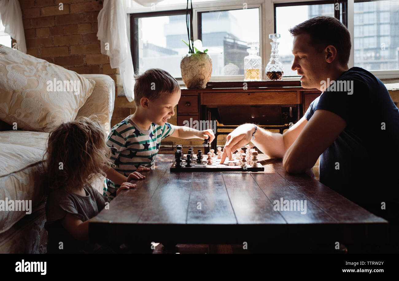 Vue latérale du père jouer aux échecs avec les enfants sur la table à la maison Banque D'Images