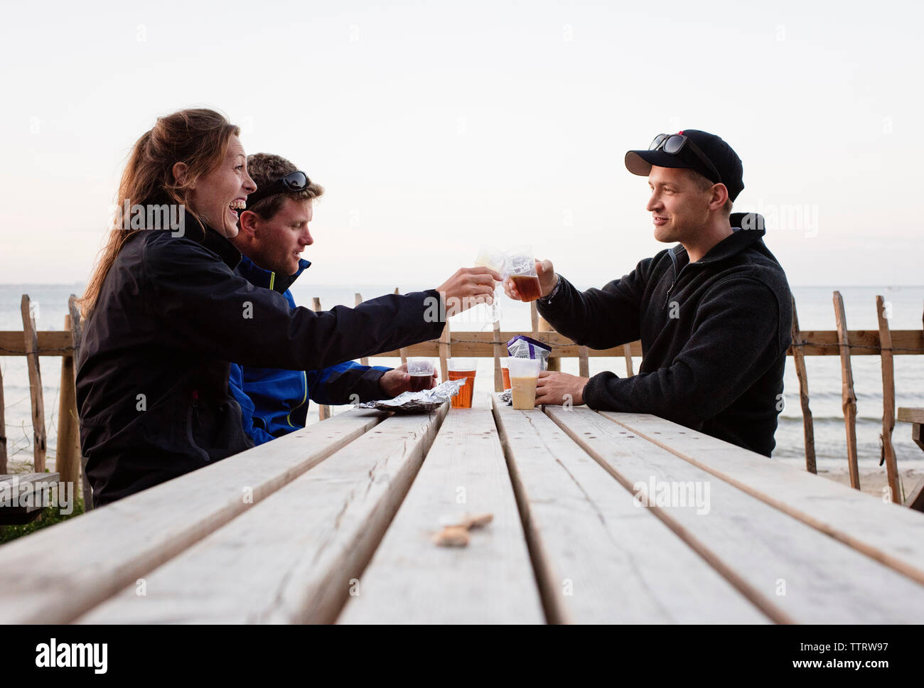 Friends toasting drinks assis à table contre ciel clair Banque D'Images