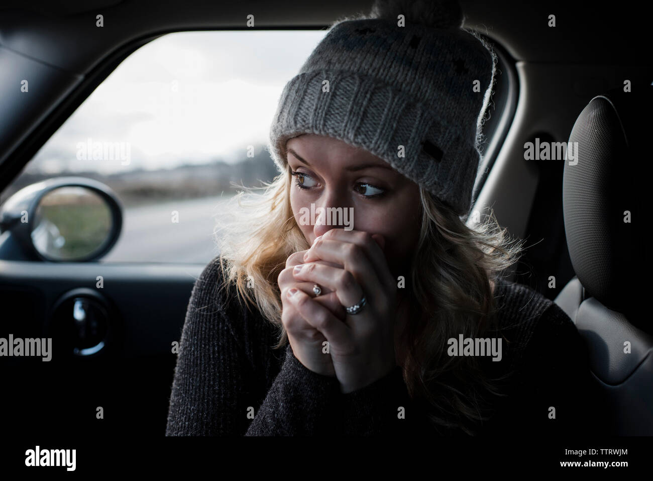 Close-up of woman with hands clasped looking away while sitting in car Banque D'Images