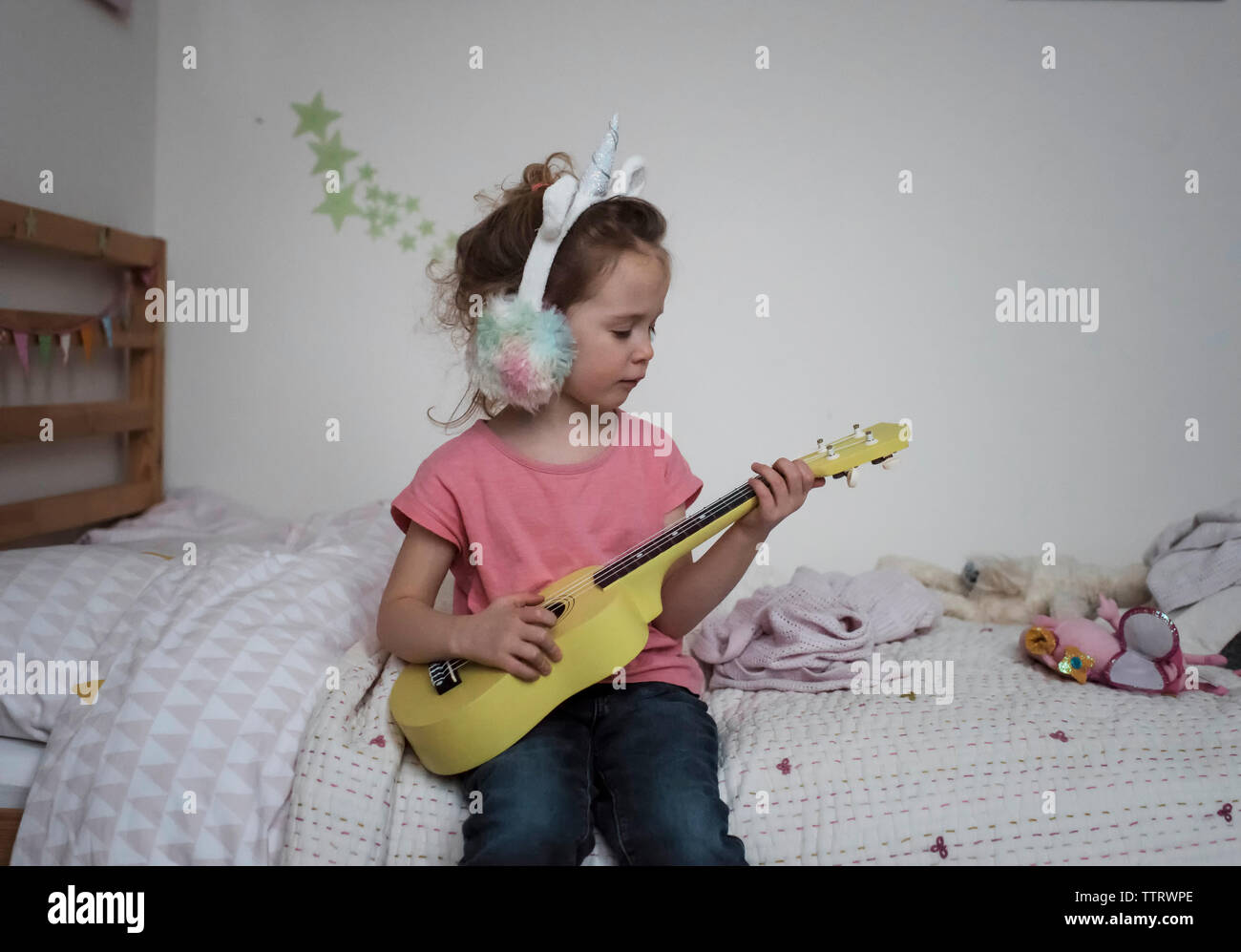 Young Girl playing ukulele à visage tenue que dans la chambre unicorn Banque D'Images