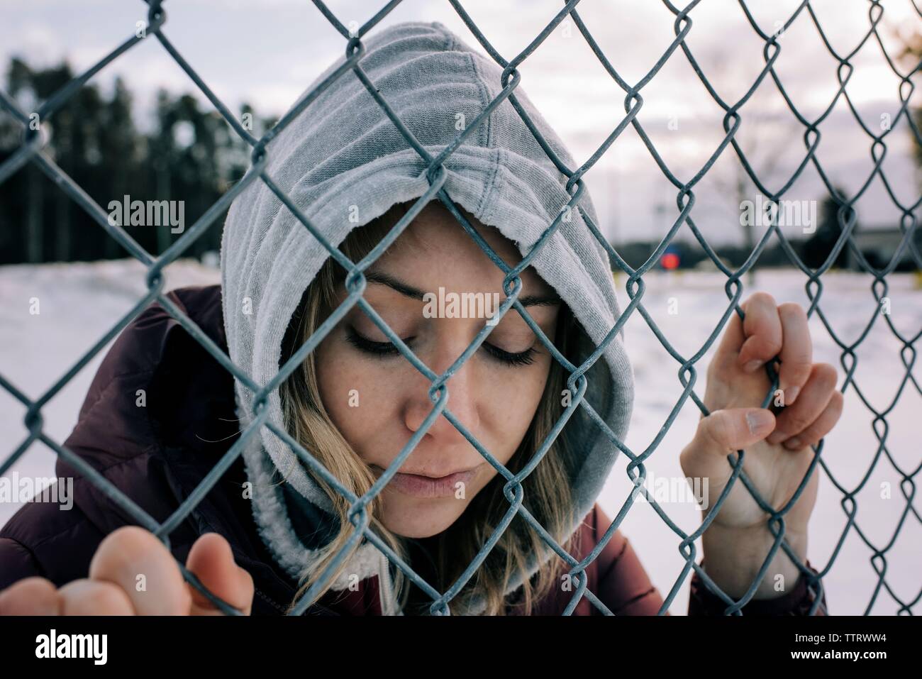 Portrait de femme tenant une clôture métallique avec son capot en hiver Banque D'Images