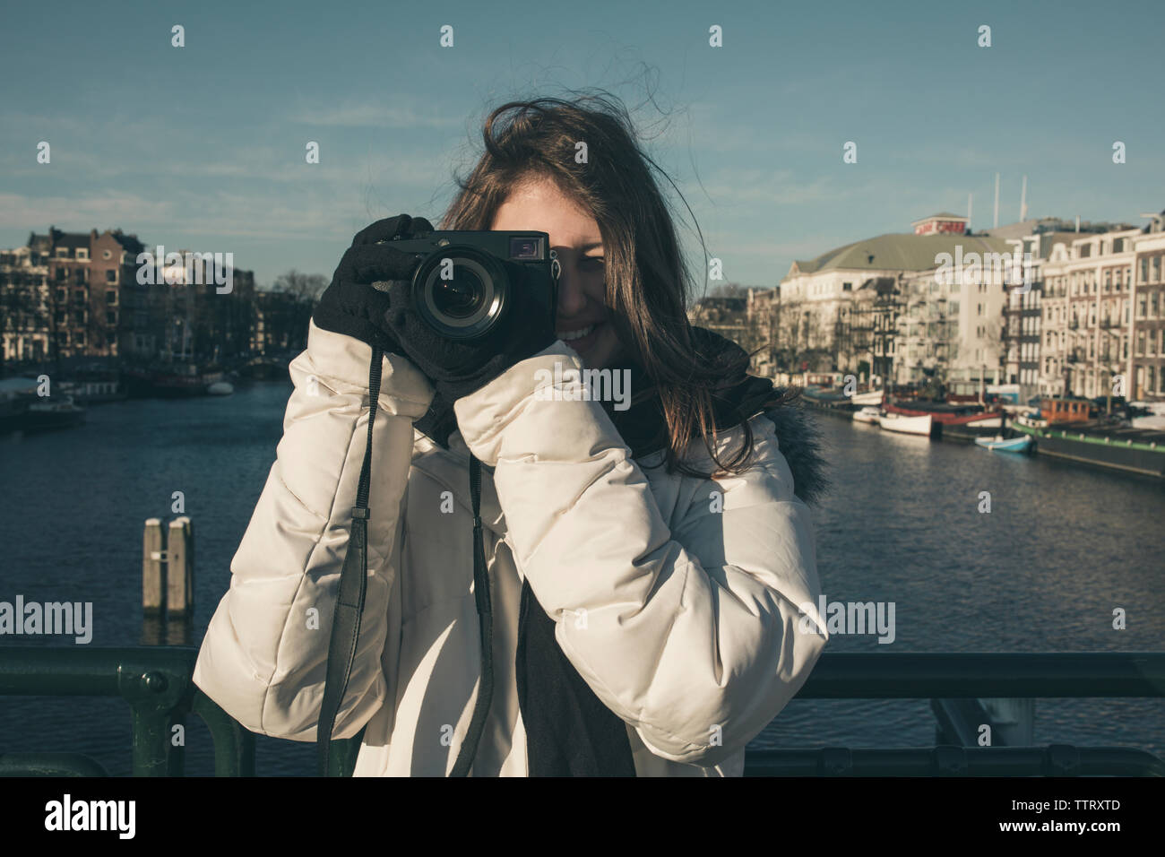 Smiling young woman photographing avec caméra contre canal en ville Banque D'Images