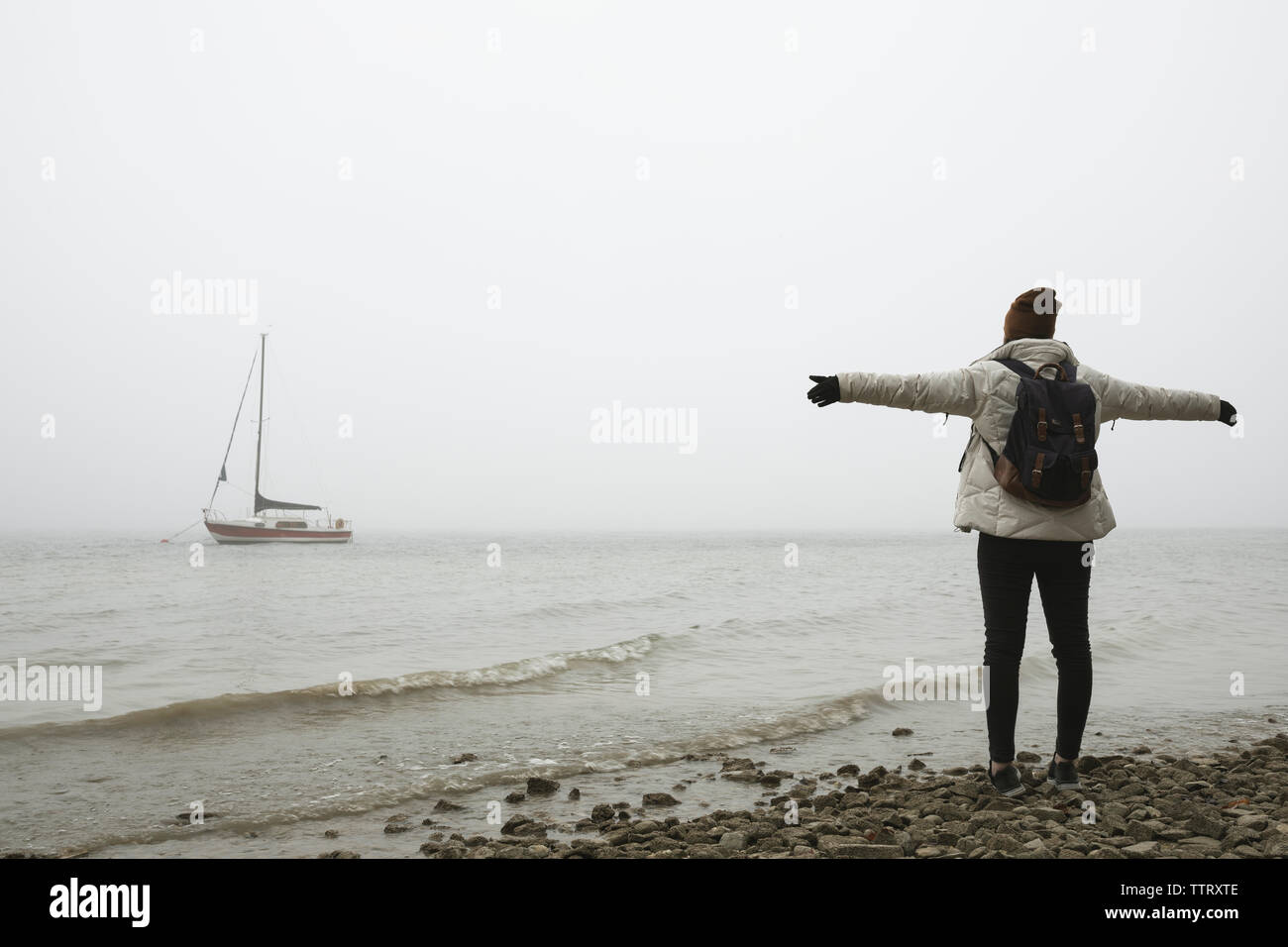 Young woman with arms outstretched standing at beach against clear sky en hiver Banque D'Images