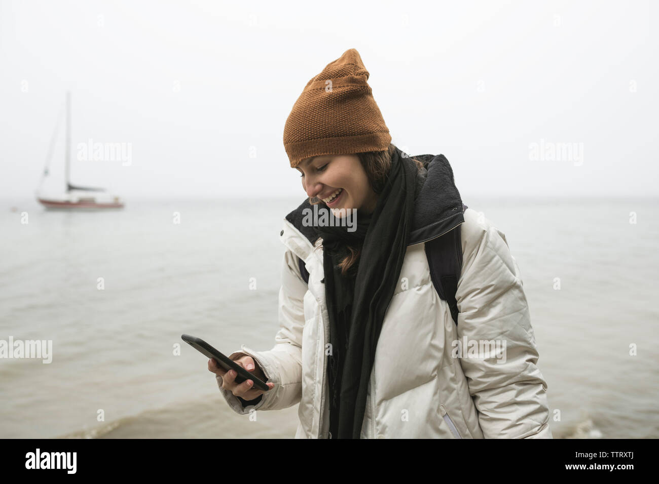 Smiling young woman using smart phone at beach pendant l'hiver Banque D'Images