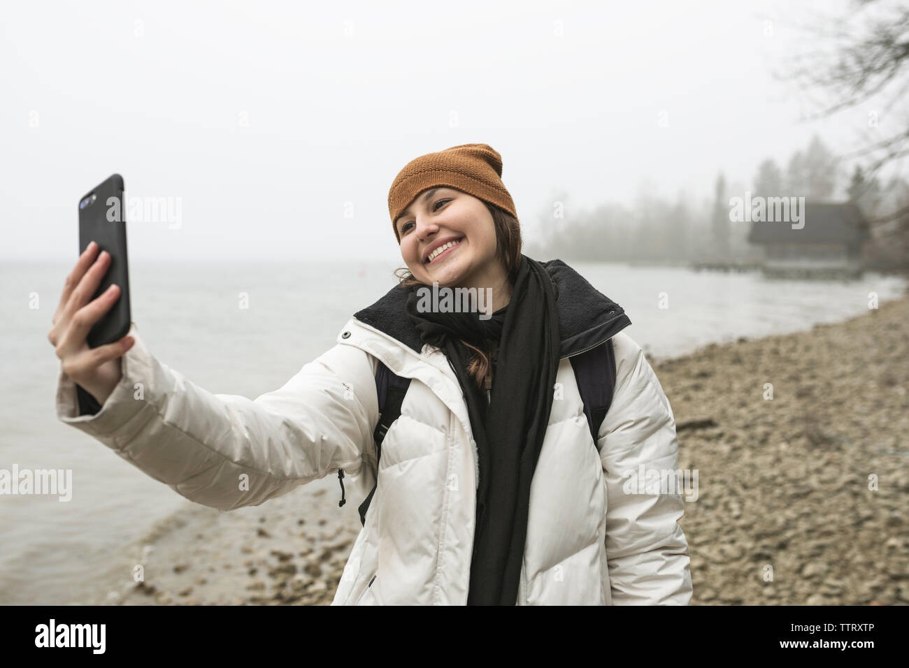Jeune femme en tenant avec selfies smart phone at beach pendant l'hiver Banque D'Images