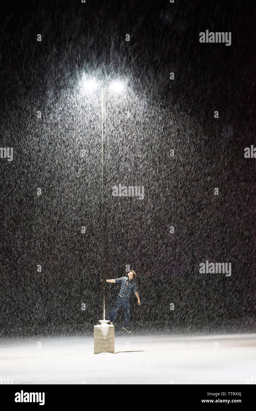 Teenage boy standing par la lumière de la rue pendant la nuit de neige Banque D'Images