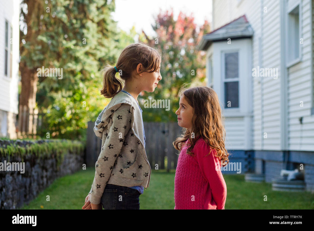 Vue latérale des sœurs à l'un l'autre tout en se tenant en arrière-cour Banque D'Images