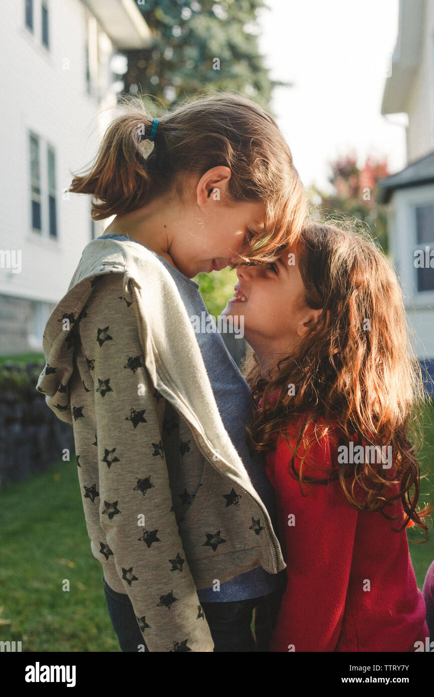 Vue latérale des sœurs espiègles se frottant le nez tout en se tenant en arrière-cour Banque D'Images