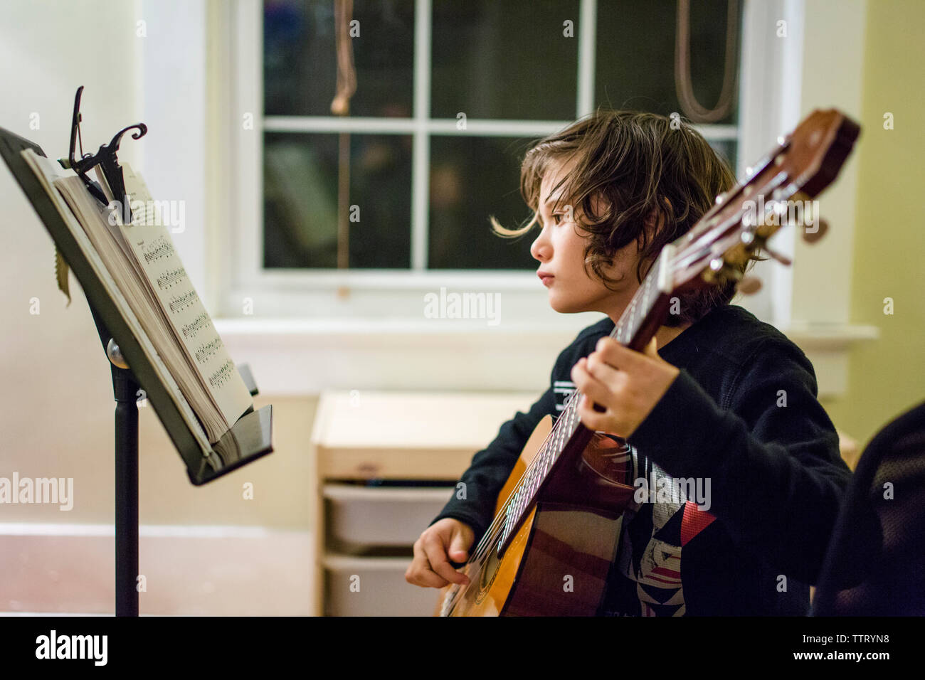 Un jeune garçon guitare pratique la nuit en face de la fenêtre Banque D'Images