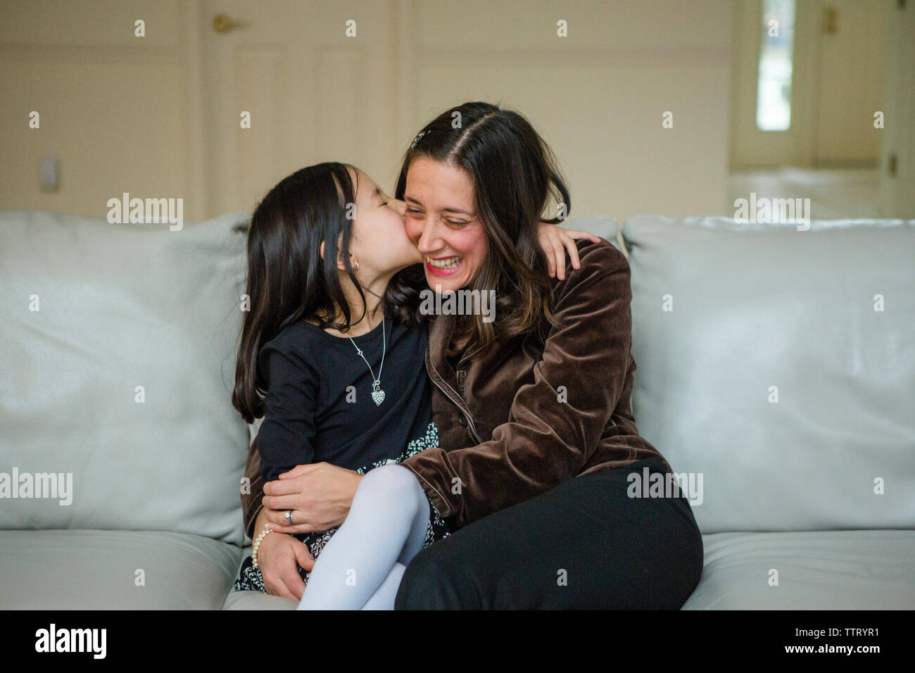 Loving mother and daughter hugging on sofa at home Banque D'Images