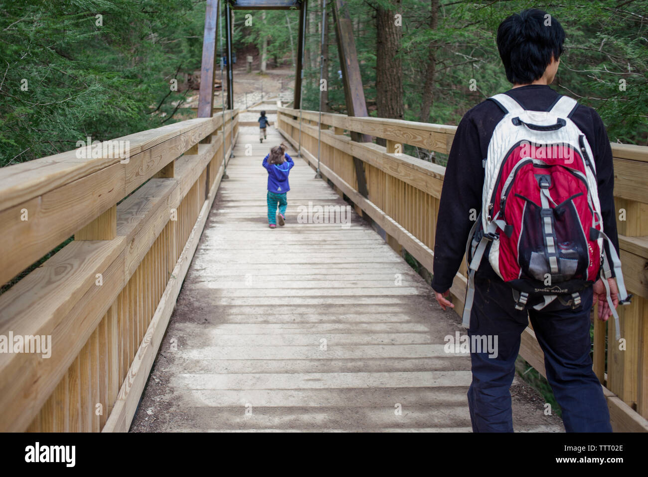 Un père traverse un long pont en bois en bois avec deux petits enfants Banque D'Images