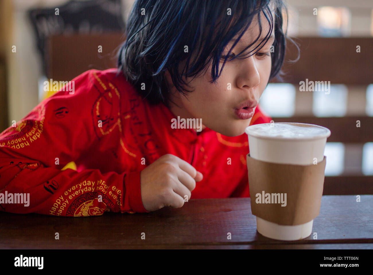 Un bel enfant assis à une table de café souffle sur une tasse de cacao chaud Banque D'Images