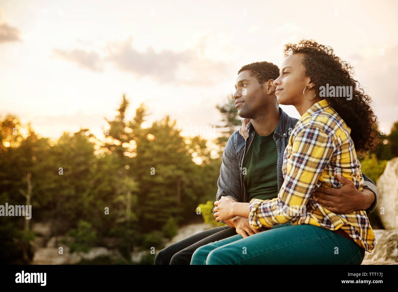 Affectionate couple sur rock contre le ciel au coucher du soleil Banque D'Images