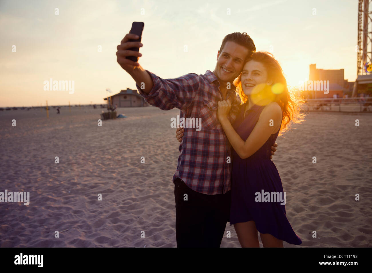 Jeune couple en tenant debout sur le sable selfies pendant le coucher du soleil Banque D'Images