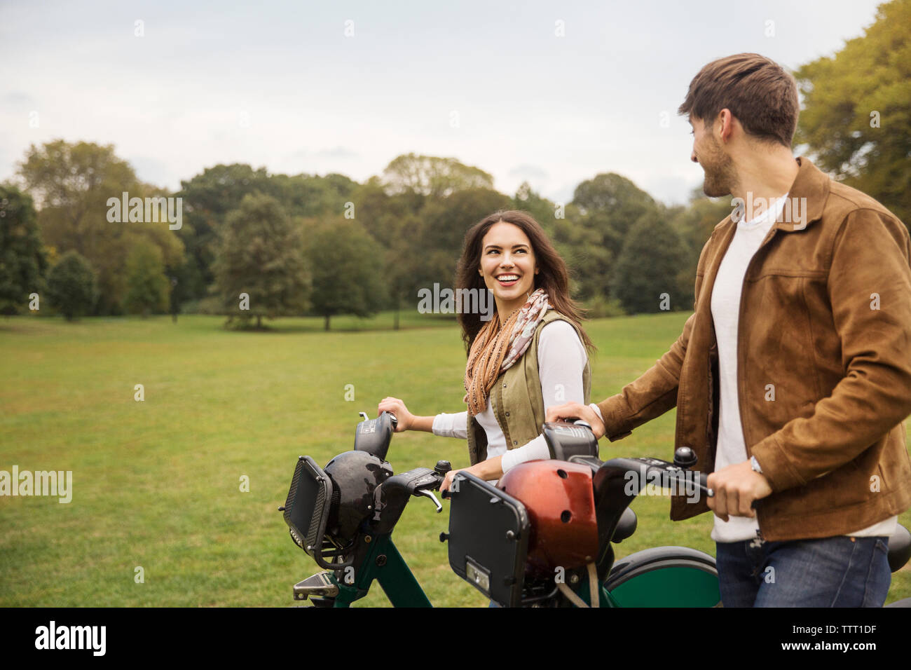 Couple heureux de parler tout en marchant avec des vélos en stationnement Banque D'Images