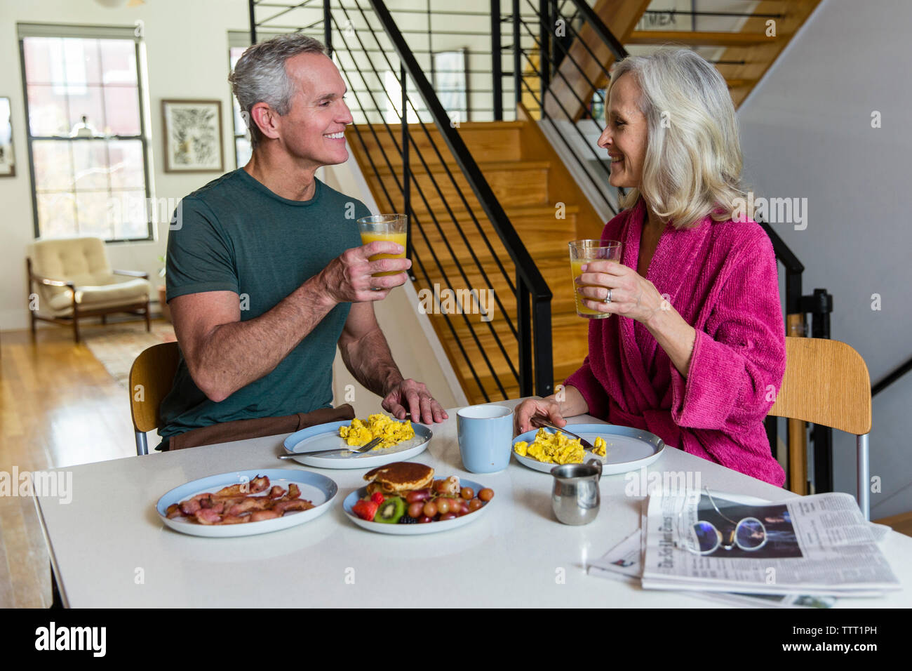 Smiling couple holding jus tout en regardant face à face à une table à manger Banque D'Images