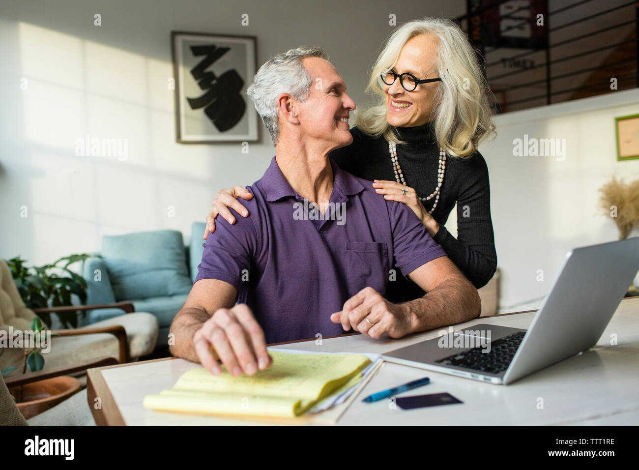 Smiling couple looking face à face tout en utilisant un ordinateur portable à la maison Banque D'Images