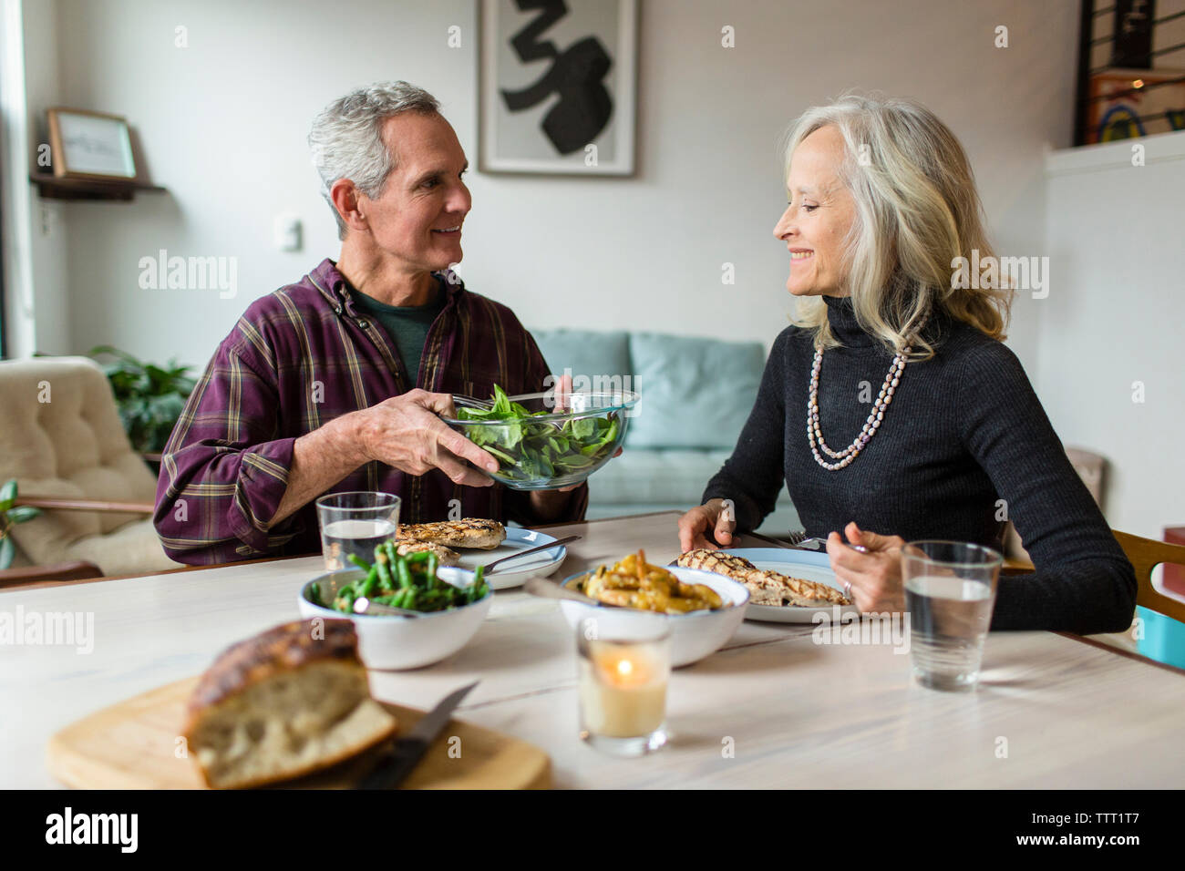 Smiling man giving bol de légumes verts à la femme tout en étant assis à table à manger Banque D'Images