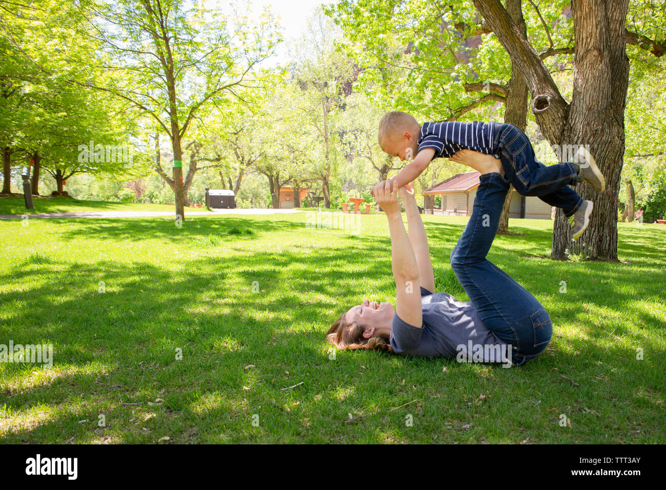 Vue latérale d'équilibrage mère ludique fils sur les jambes du park Banque D'Images
