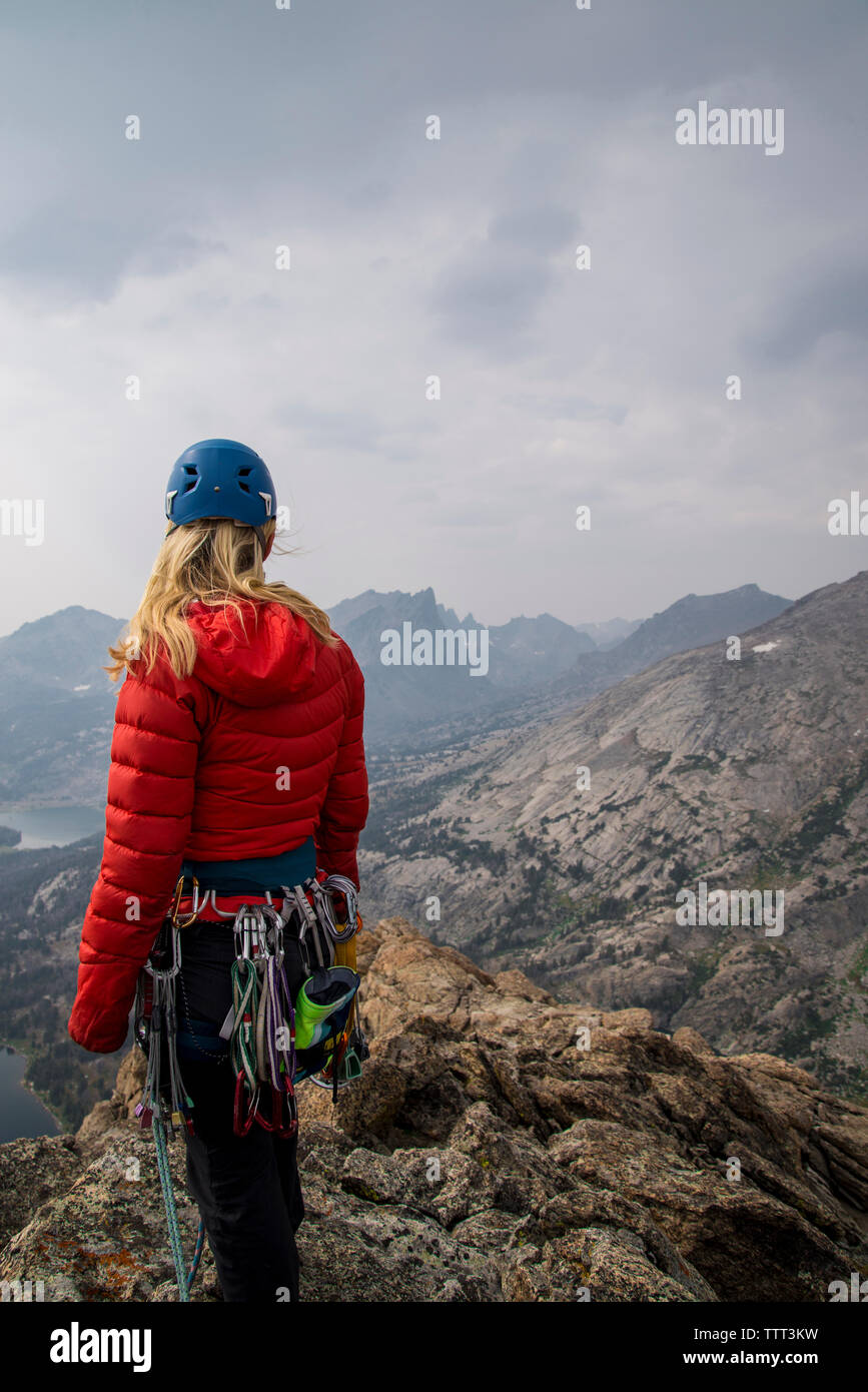 Female hiker avec mountain climbing equipment looking at view en se tenant sur le falaise against sky Banque D'Images