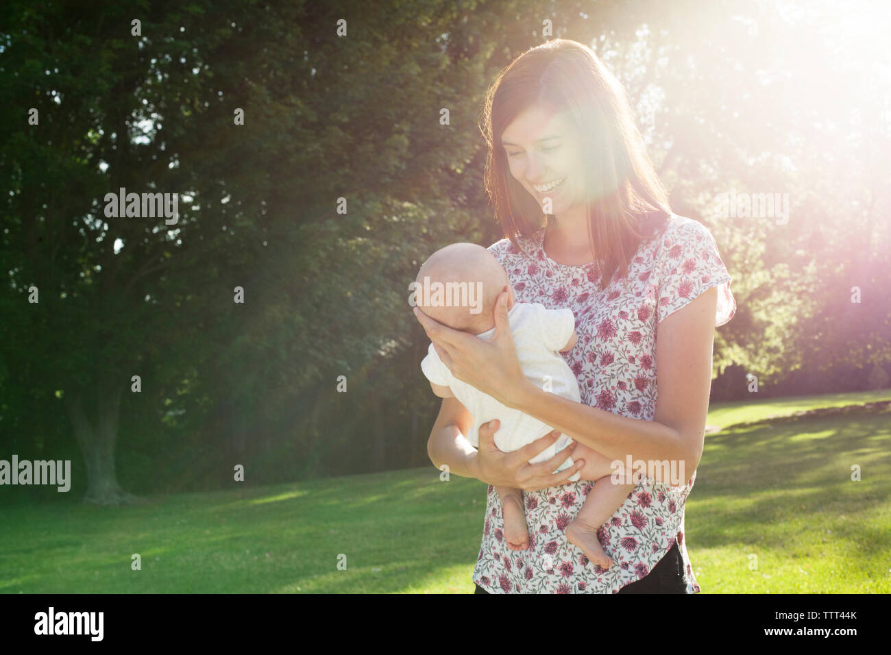 Happy mother carrying baby tout en se tenant au parc sur sunny day Banque D'Images