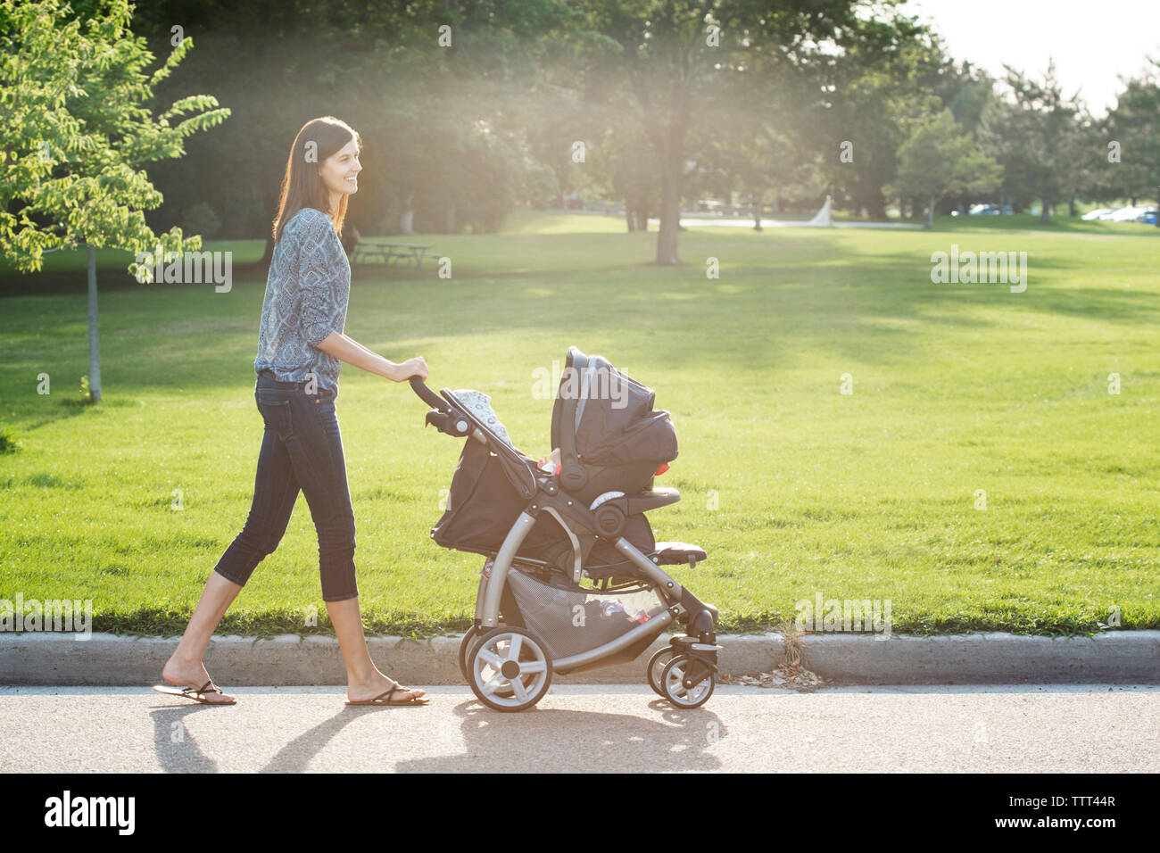 Vue latérale du smiling woman walking avec poussette de bébé sur street at park Banque D'Images