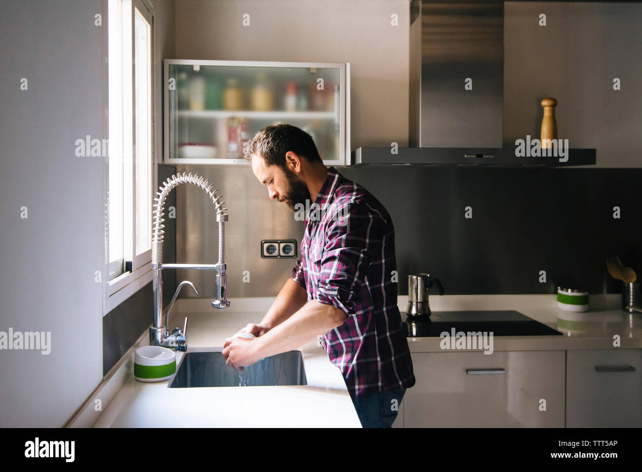 Homme avec barbe et chemise à carreaux lave-vaisselle à la maison. Banque D'Images