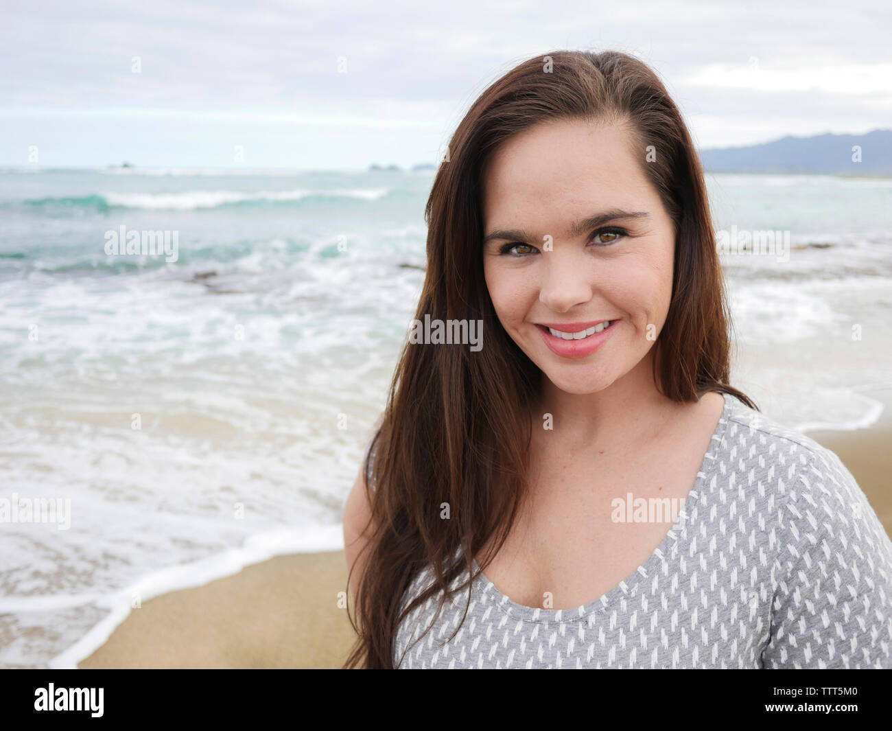 Portrait of happy woman standing at beach against cloudy sky Banque D'Images