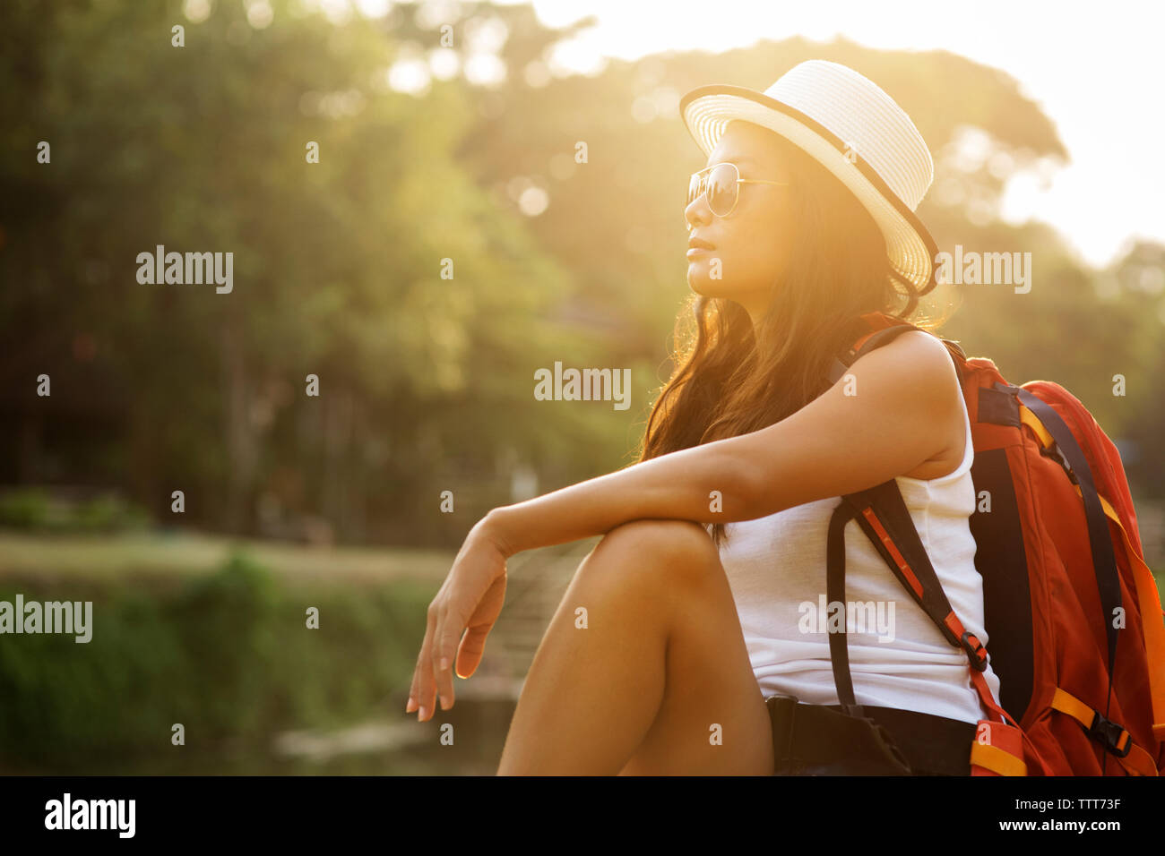 Backpacker femelle portant chapeau de soleil tout en vous relaxant au soleil sur les berges Banque D'Images