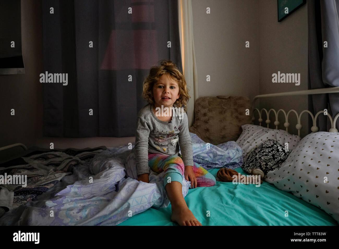Portrait of cute girl sitting on bed at home Banque D'Images